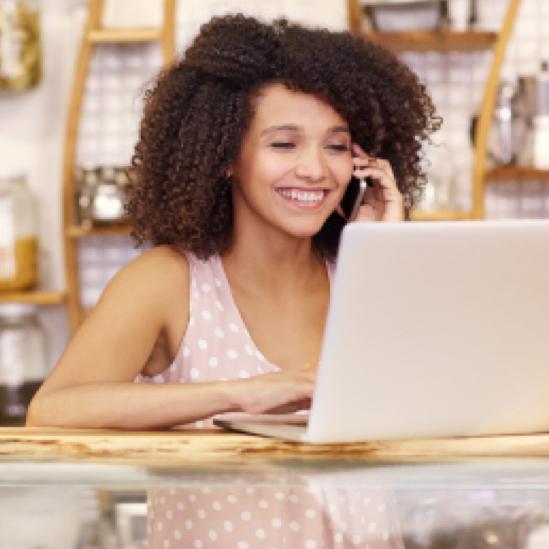 Smiling woman talking on the phone while browsing on her laptop